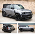Load image into Gallery viewer, Silver Land Rover Defender 110 L663, fitted with Barugzai Falcon bodykit, parked on a road with a brick wall background. Fitted with Barugzai Sabre 22" alloy wheels in Gloss Black