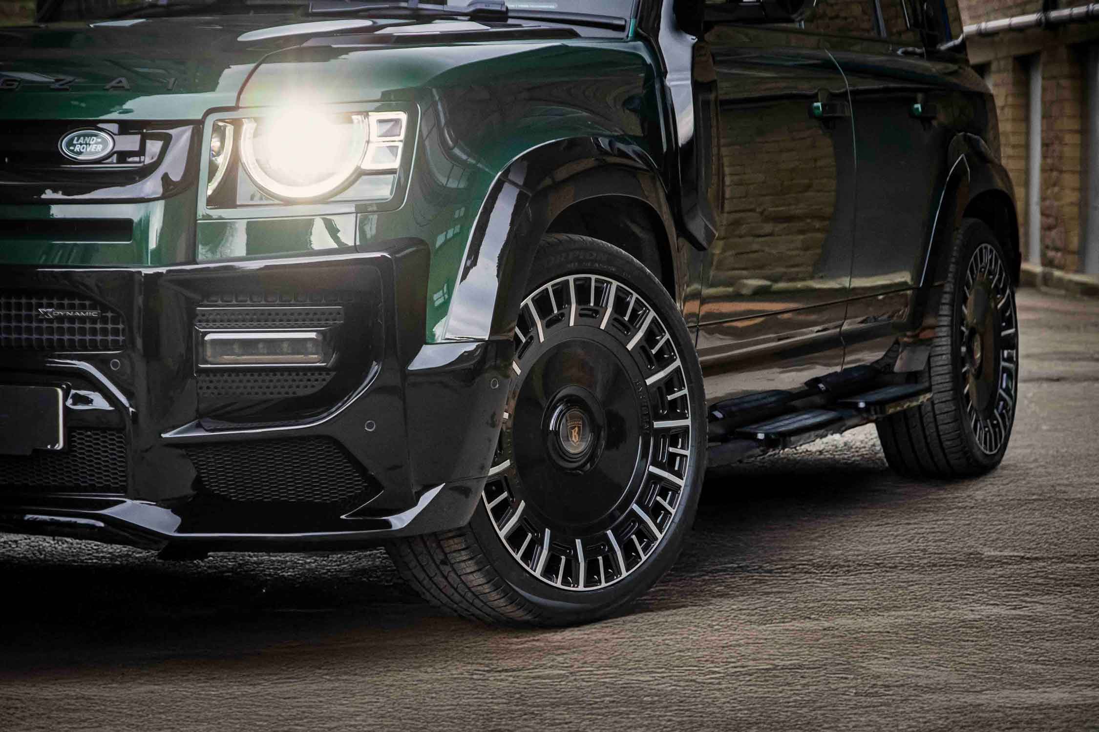 Close-up of a green Land Rover Defender 110 L663, fitted with Barugzai Falcon. Detailed view of the front wheel and grille. Barugzai Monoblock Forged 23