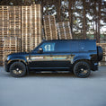 Load image into Gallery viewer, Side angle of Land Rover Defender parked on pavement with wooden crates behind, fitted with Barugzai gloss black 22‑inch wheels
