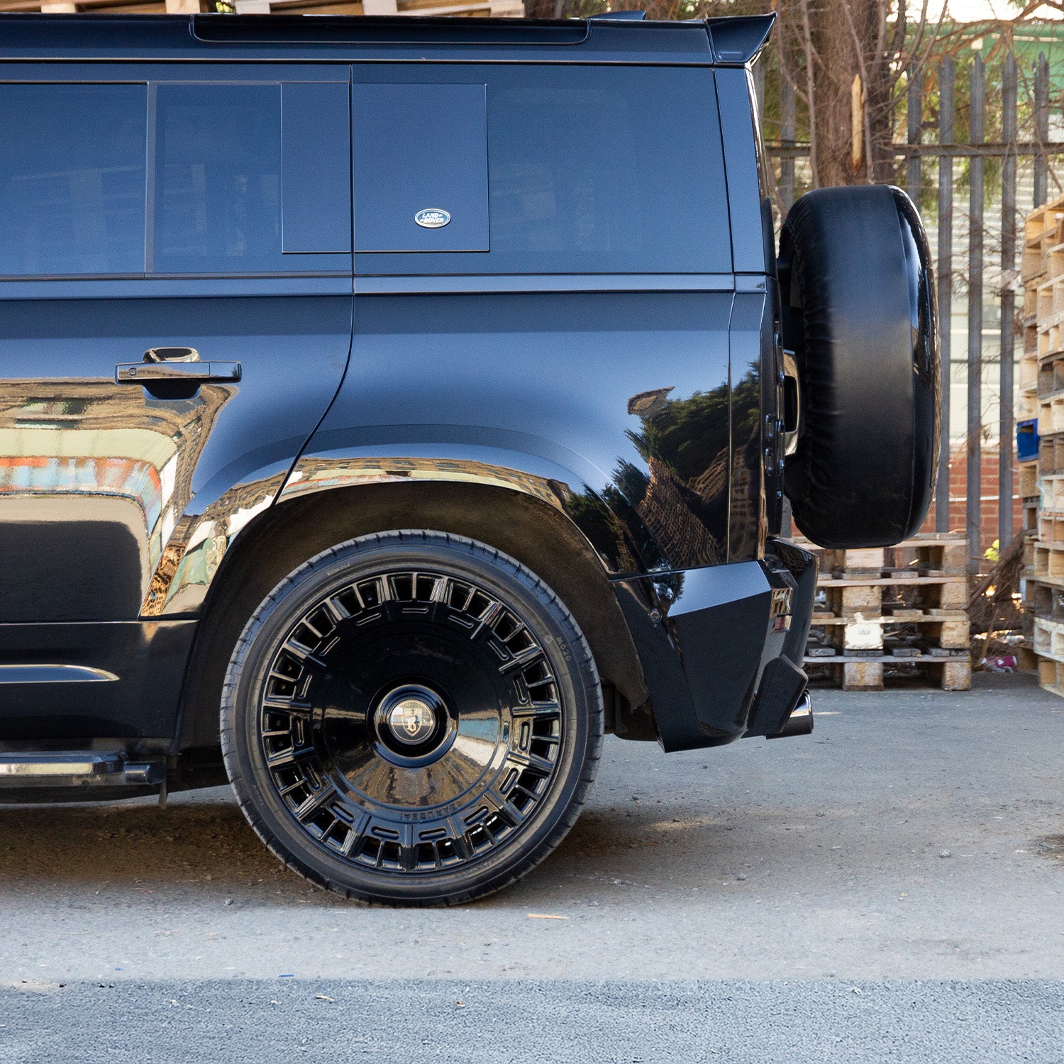 Side close‑up of rear Barugzai 22‑inch gloss black wheel on Defender, showing spoke profile and brake visibility
