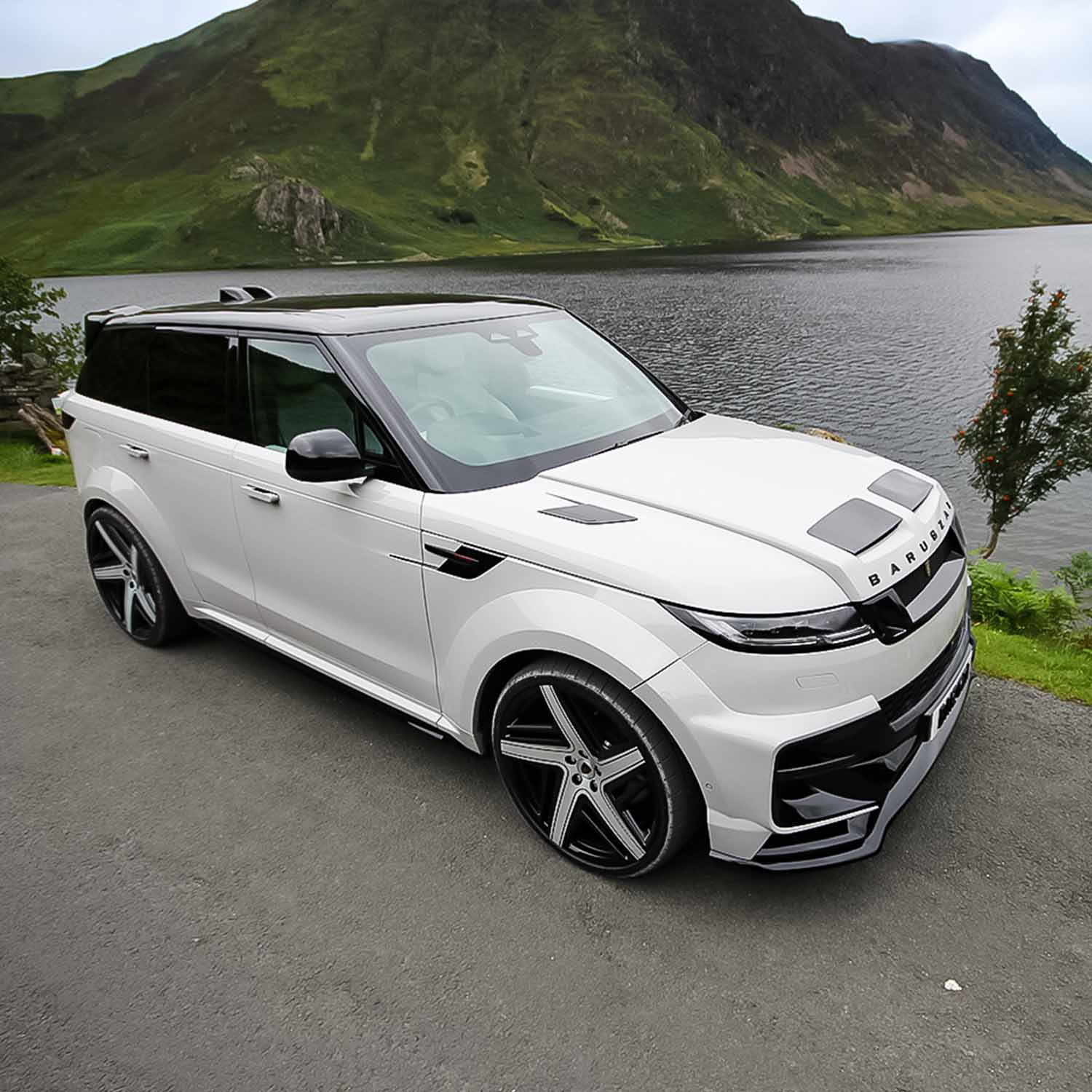 Top front‑quarter angle of Range Rover Sport L461 with Barugzai Raptor bodykit overlooking a lake and green hills.
