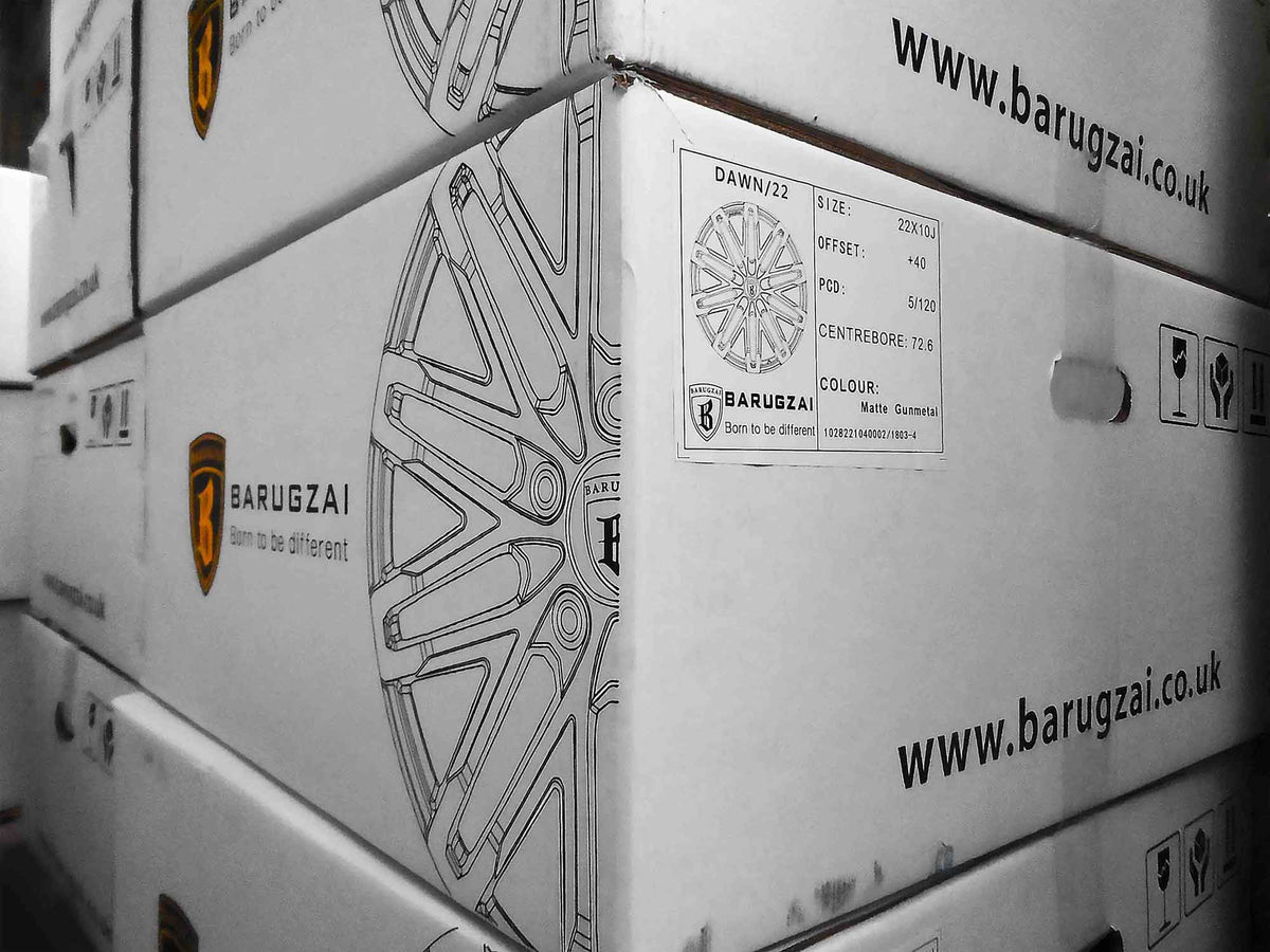 Stack of white Barugzai alloy wheel boxes with branding and website text on a blurred background in the Enkahnz warehouse