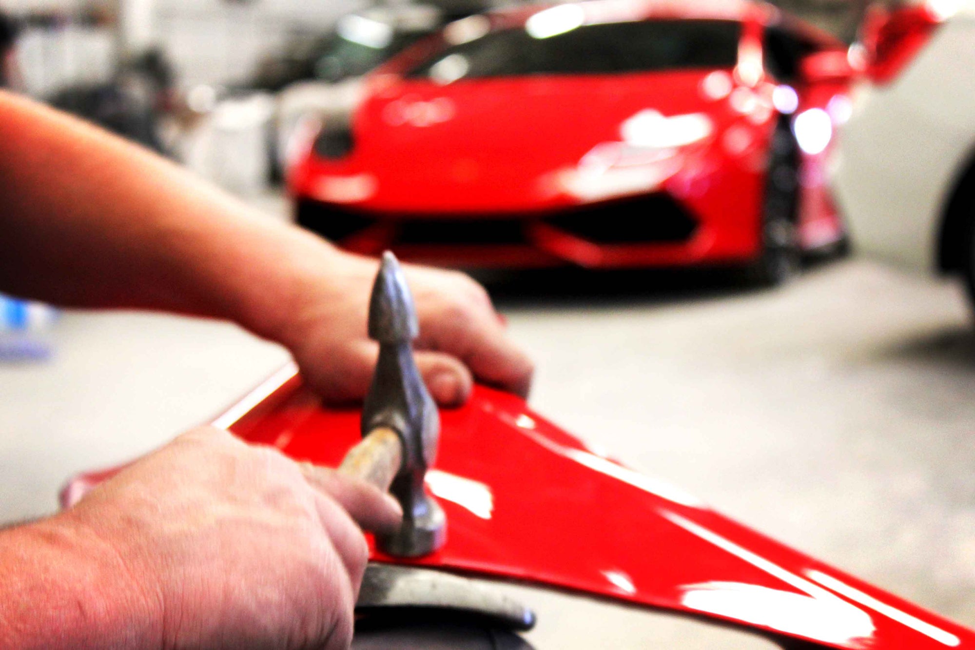 Person panel beating a front wing removed from a red Lamborghini Aventador with a blurred background of a red sports car (Lamborghini Aventador)