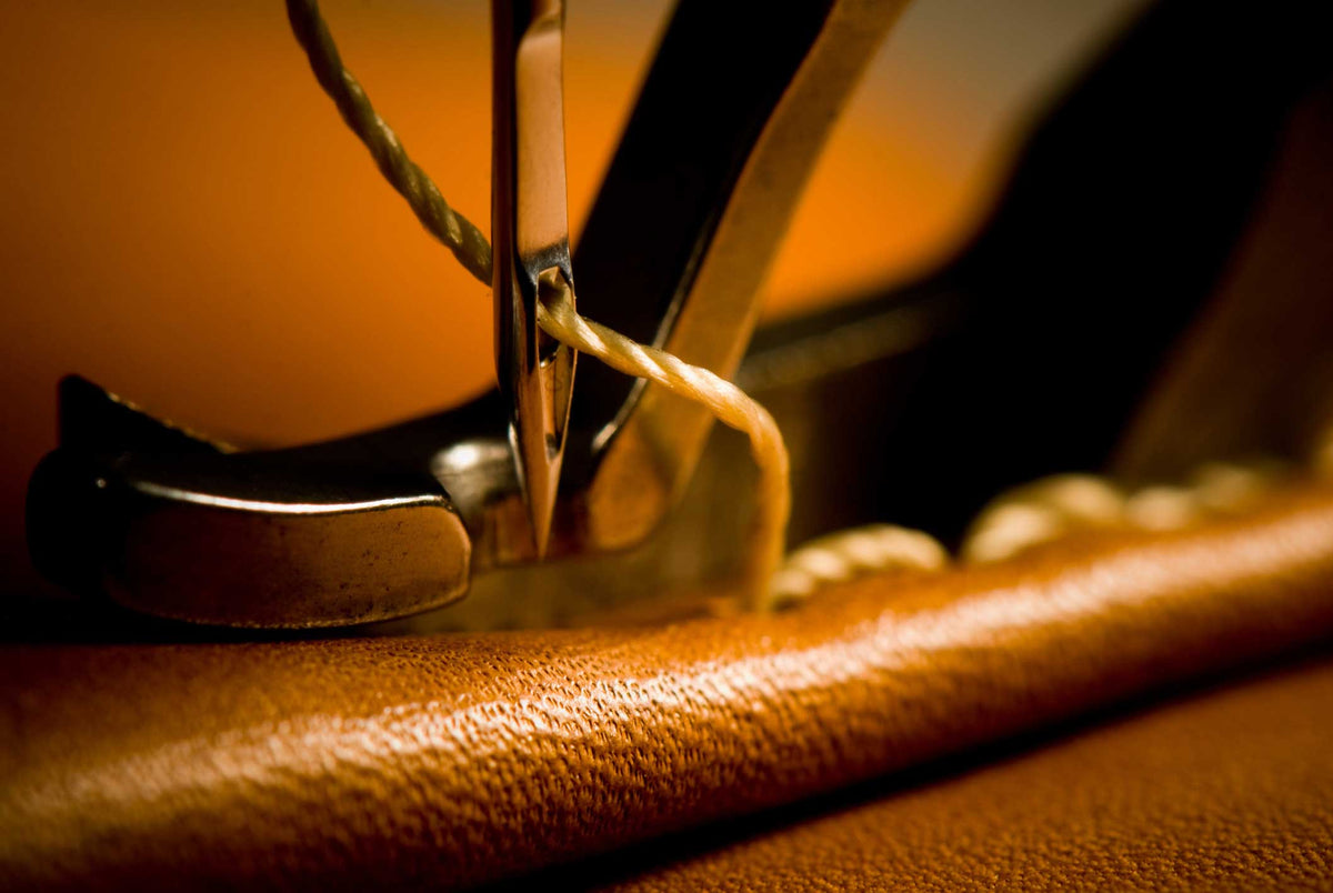 Close-up of a sewing machine needle piercing fabric with a warm color tone.