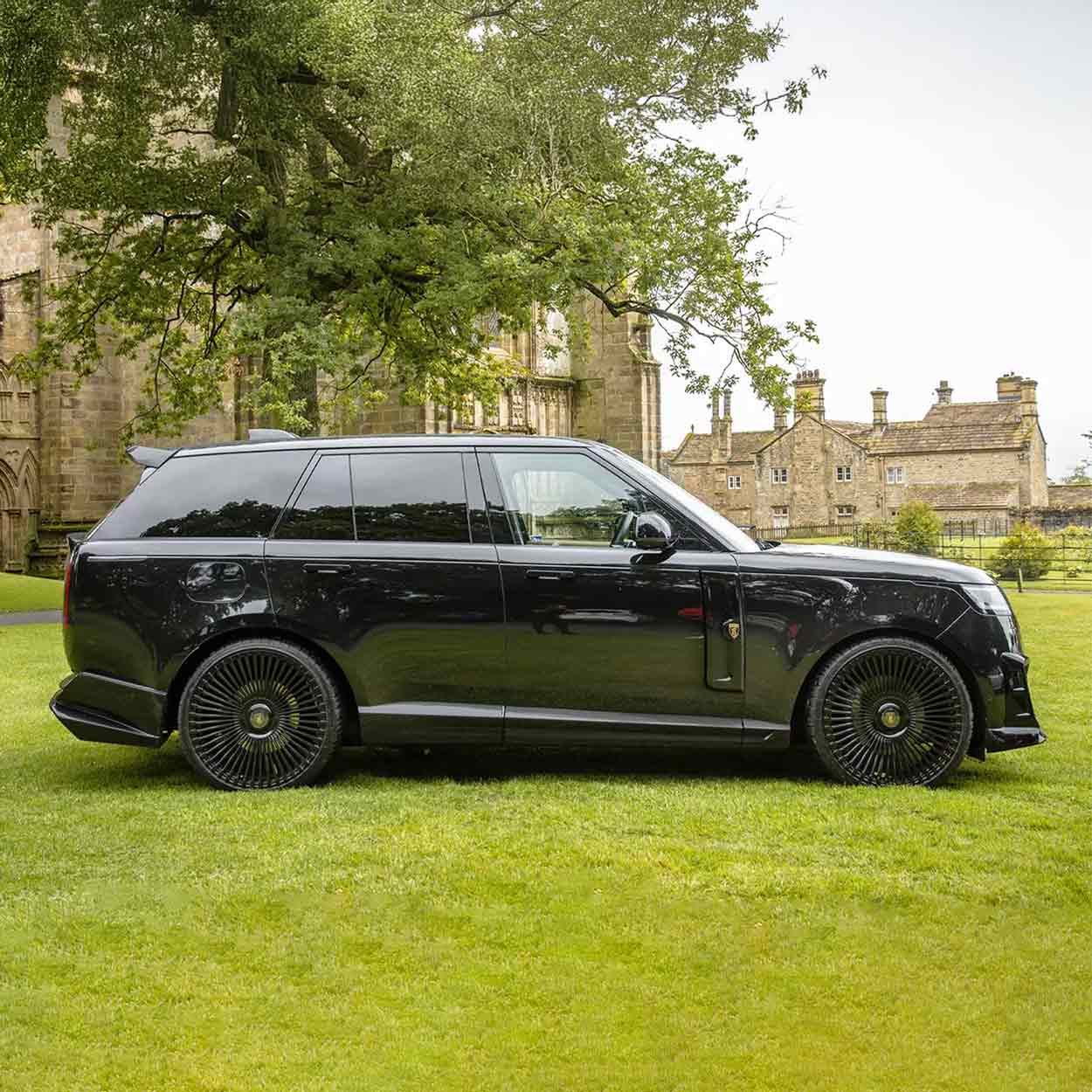 Black Range Rover L460 2022, fitted with Barugzai Nebula bodykit, shown side view, shot outside a histrorical landmark with greenery. Fitted with Barugzai Vortex Forged 24" alloy wheels in Gloss Black Polished