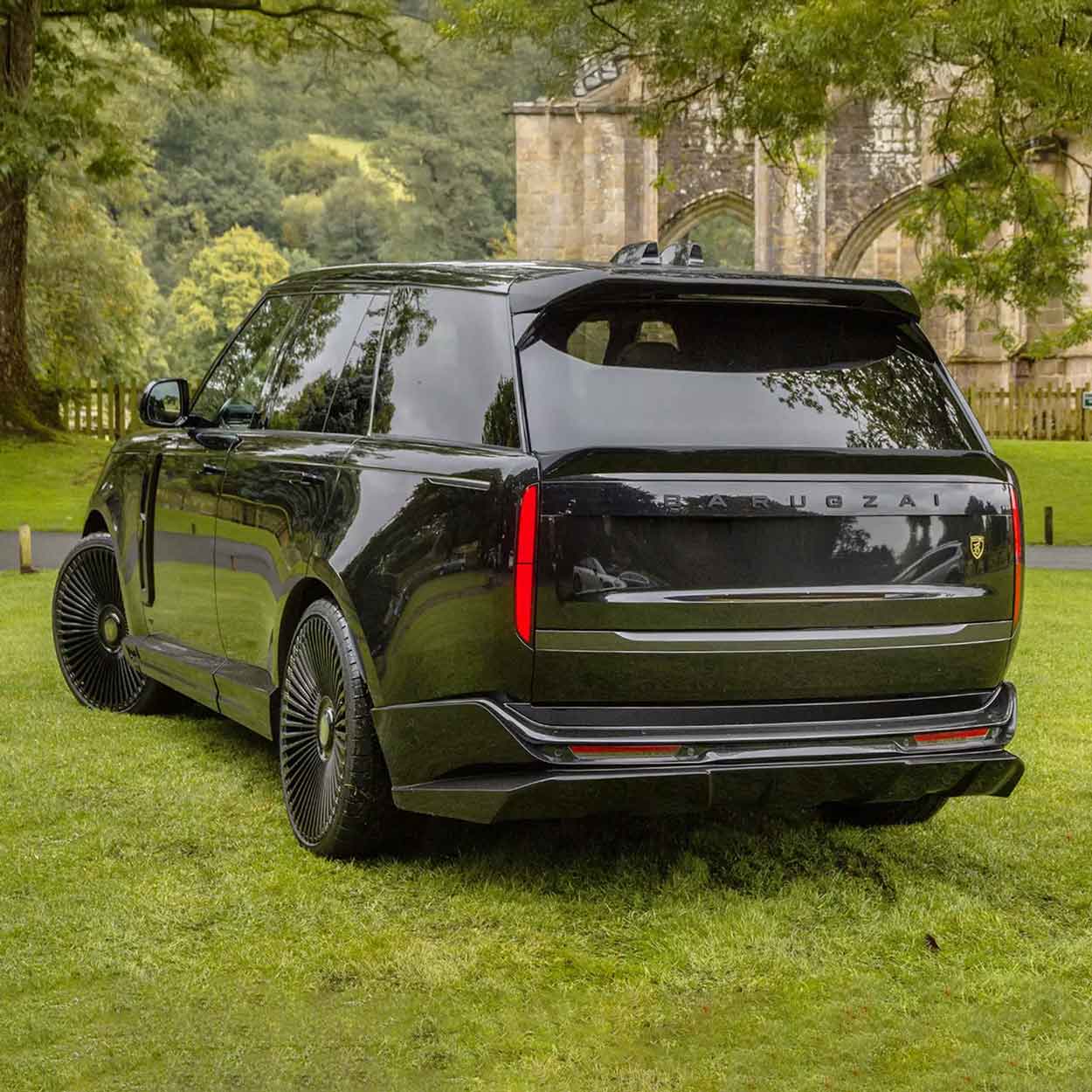 Black Range Rover L460 2022, fitted with Barugzai Nebula bodykit, shown rear quarter angle, shot outside a histrorical landmark with greenery. Fitted with Barugzai Vortex Forged 24" alloy wheels in Gloss Black Polished