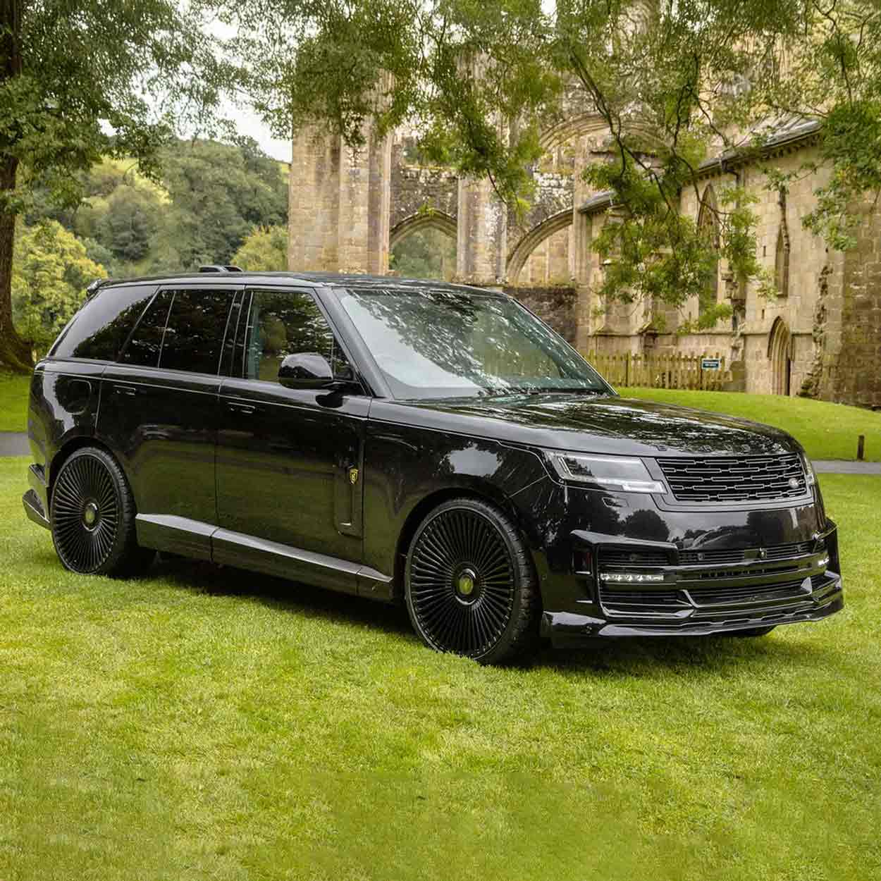 Black Range Rover L460 2022, fitted with Barugzai Nebula bodykit, shown front quarter angle, shot outside a histrorical landmark with greenery. Fitted with Barugzai Vortex Forged 24" alloy wheels in Gloss Black Polished