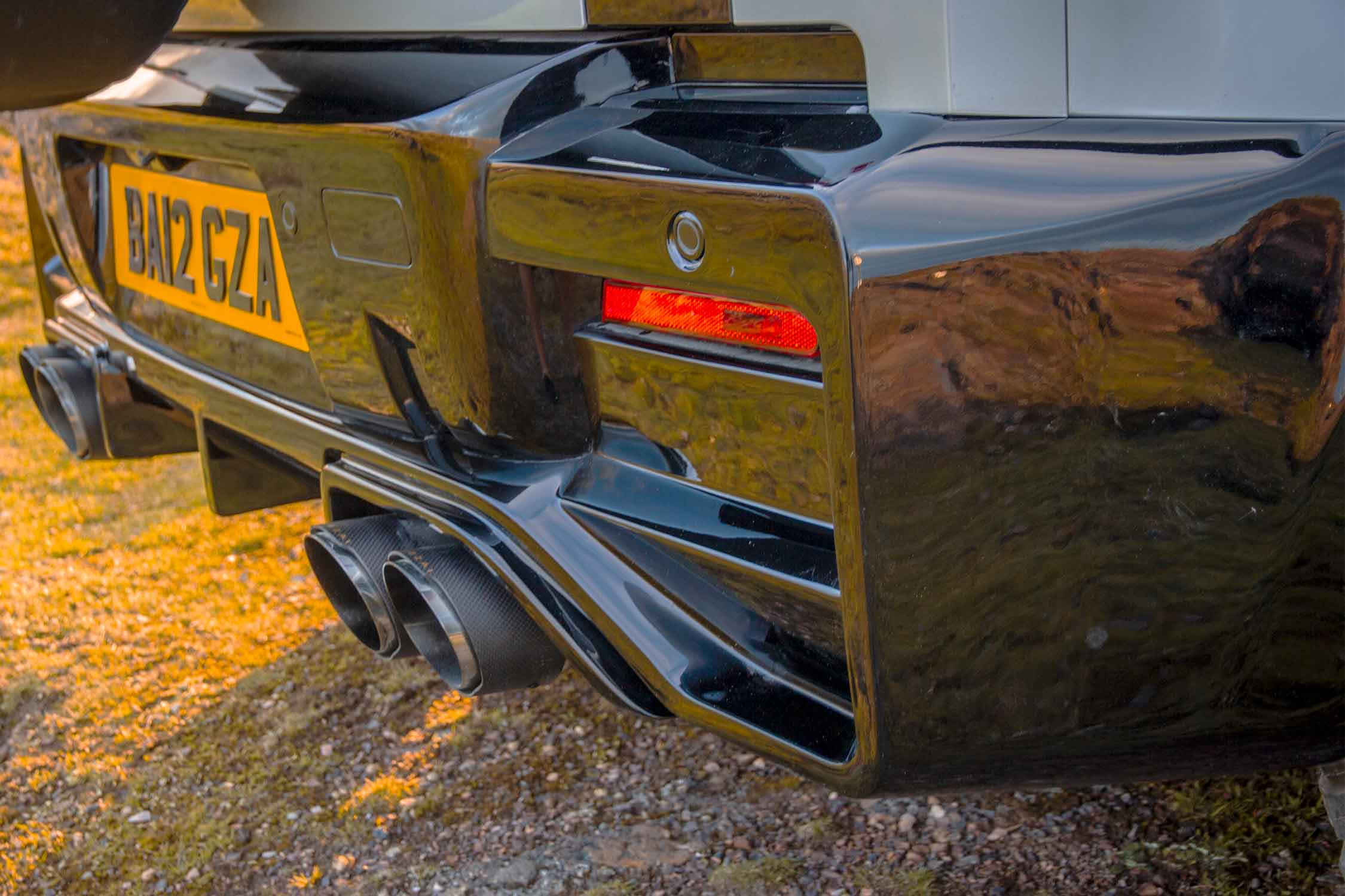 Close-up of a Land Rover Defender 110, L663 Barugzai Falcon rear diffuser and exhaust tips, in a scenic background