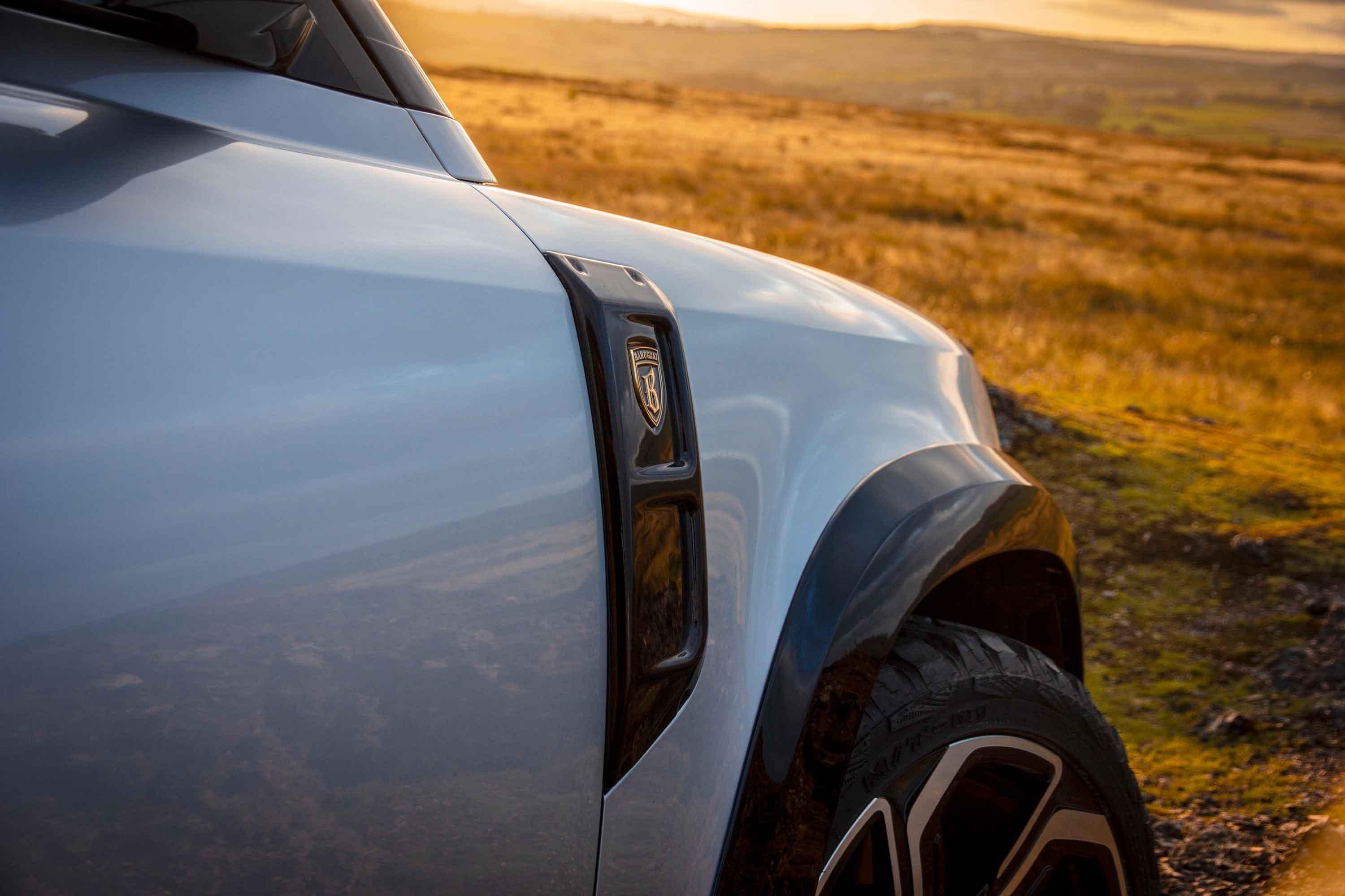 Close-up of  side vent  and front wing on a Land Rover Defender 110, Barugzai Falcon bodykit, in a scenic background. 