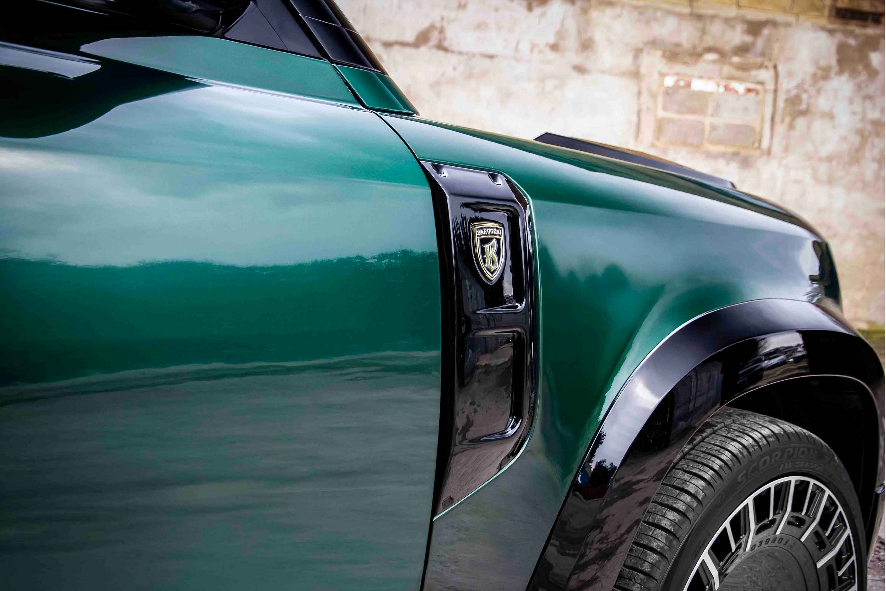 Close-up of a green Land Rover Defender 110 L663, fitted with Barugzai Falcon bodykit with a visible Barugzai side vent logo on a blurred background