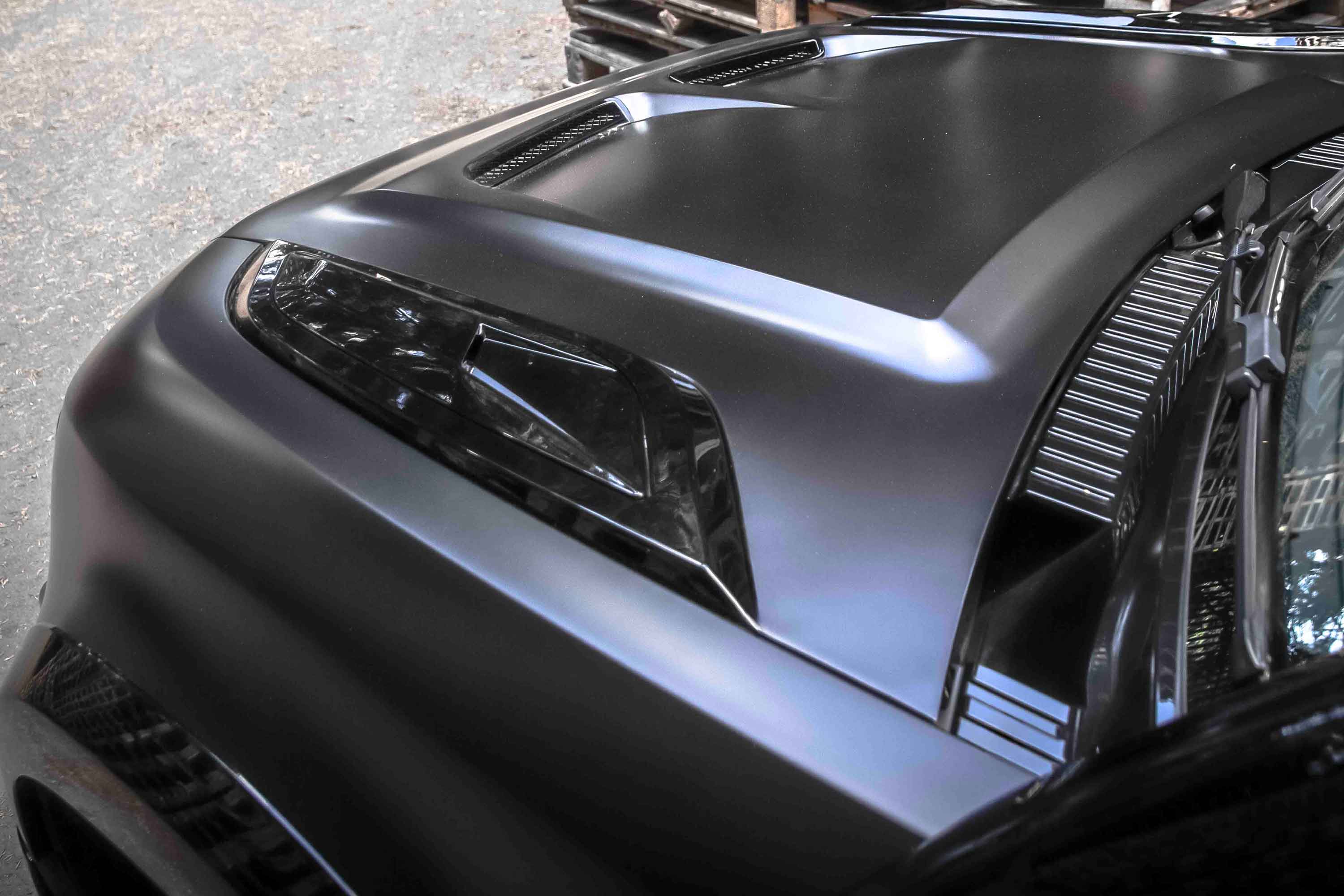 Close-up of a Land Rover Defender 110 L663, fitted with Barugzai Falcon bonnet SVR style blurred background. Matt black paint finish