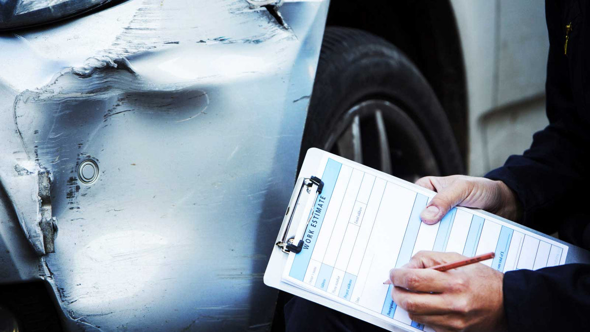 Person inspecting a car with a damaged front end, holding a form.