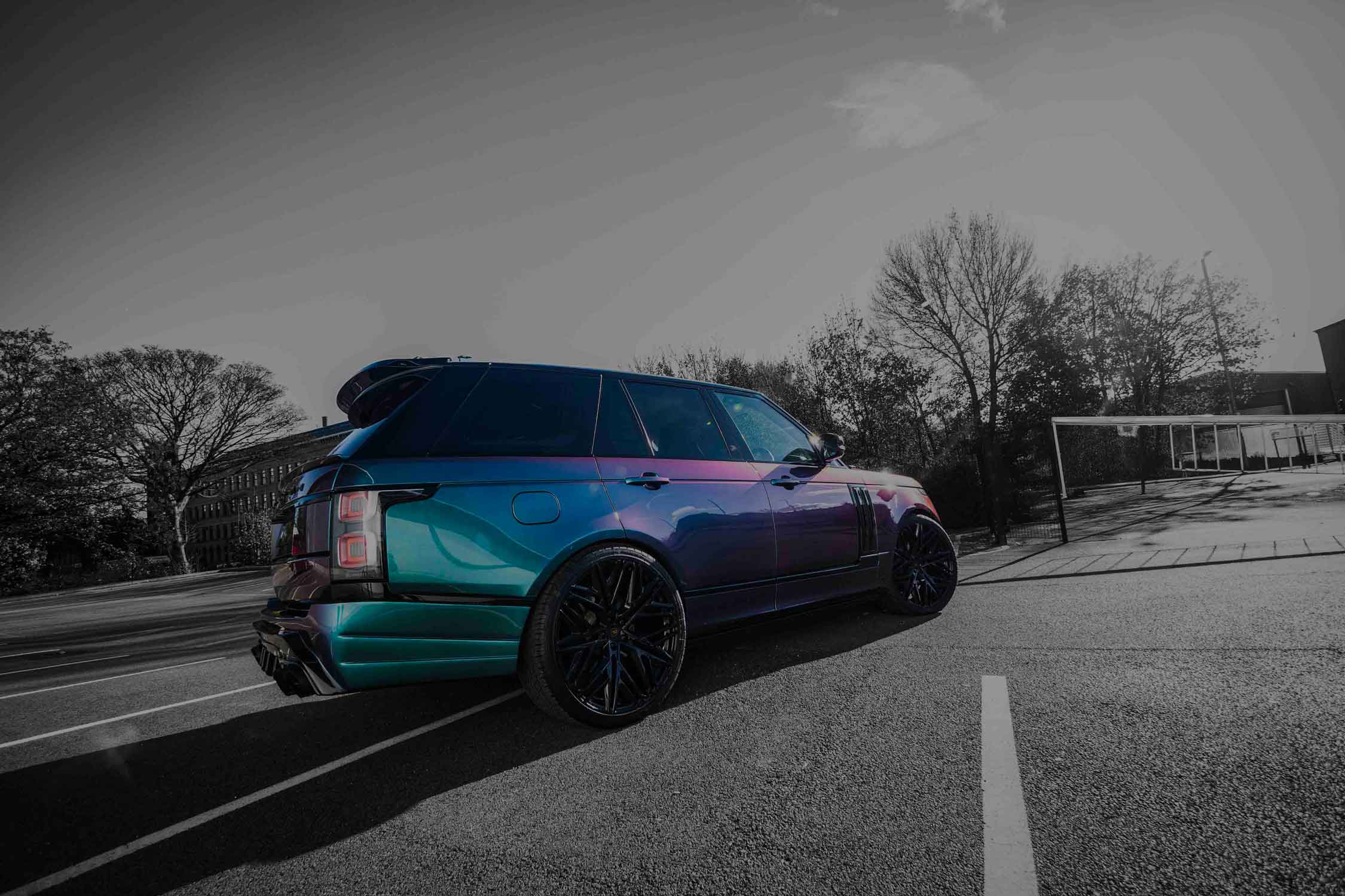 Range Rover L405 Barugzai Bison parked on a road with trees and buildings in the background, chameleon paintwork, rear view