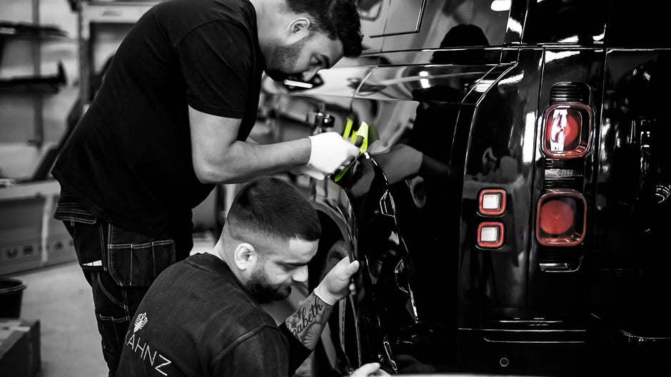Two men working on a black Land Rover Defender L663 in a garage