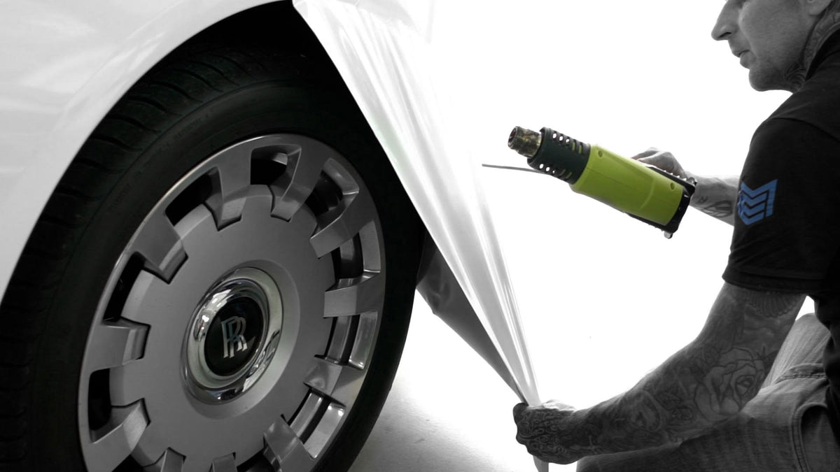 Person vinyl wrapping a Rolls Royce, applying heat gun to the vinyl, white background