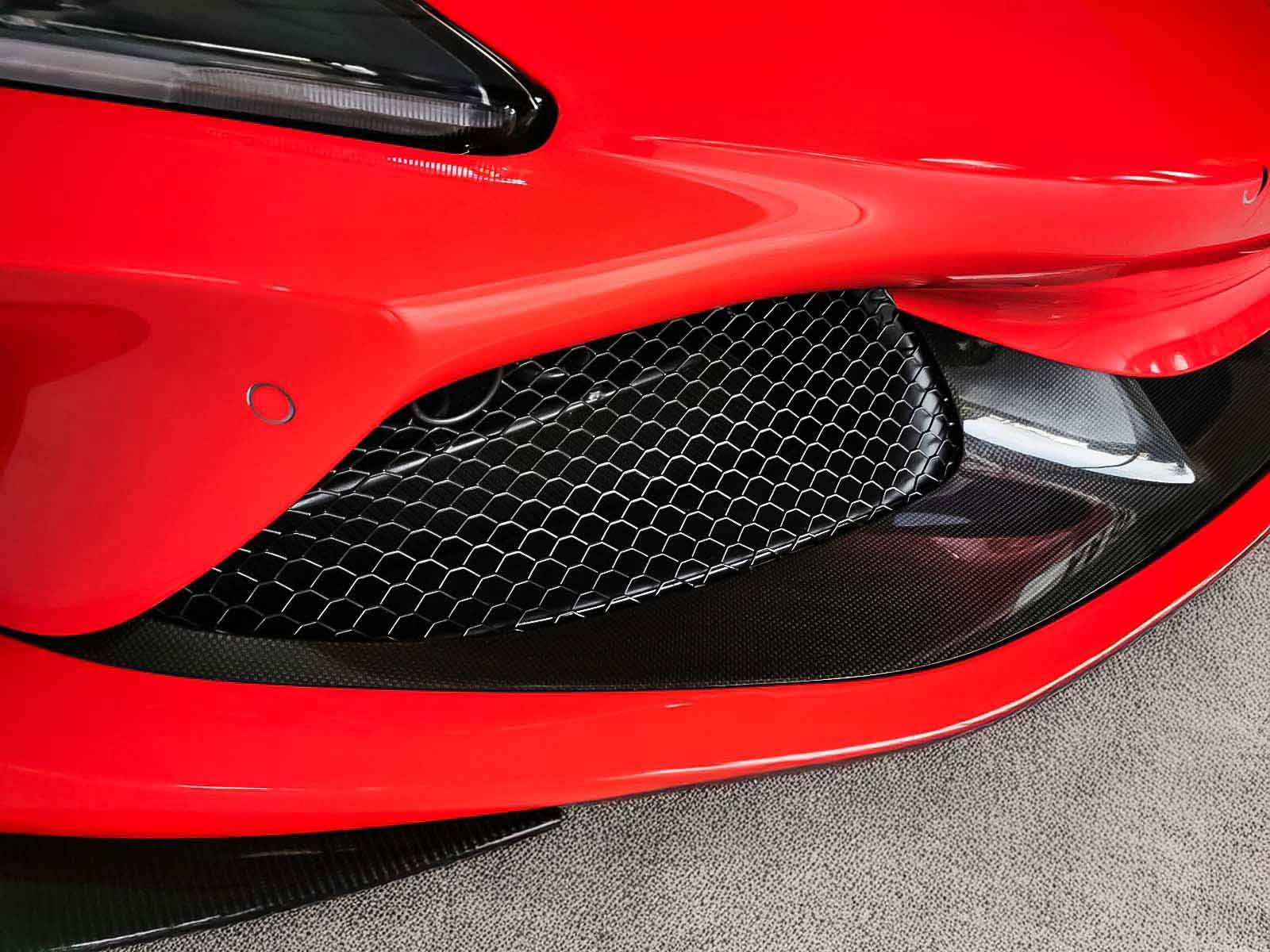 Close-up of a red Ferrari F8 tributo front grille with a black honeycomb pattern, red vinyl wrap