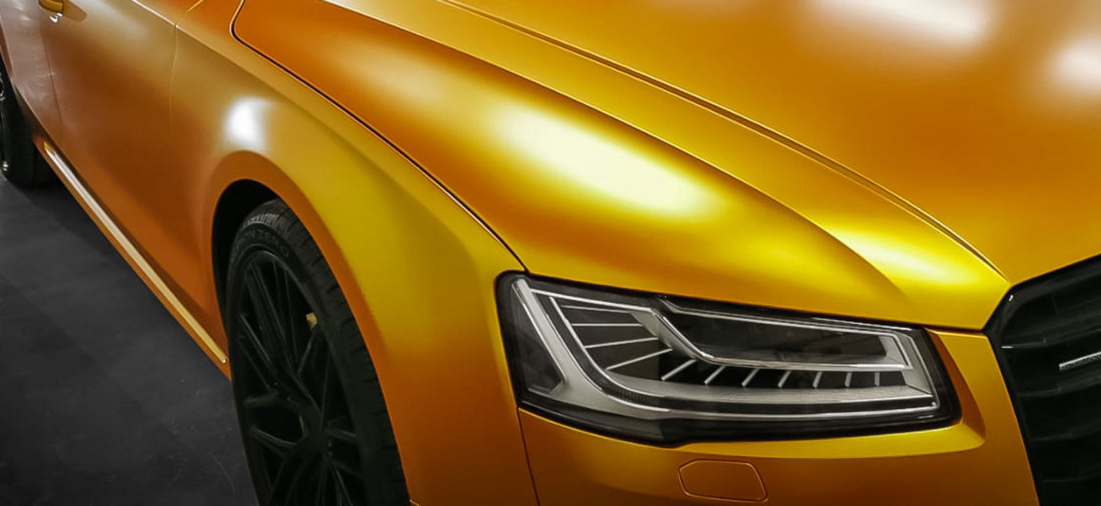 Close-up of a gold Audi A8 with a shiny vinyl wrap finish