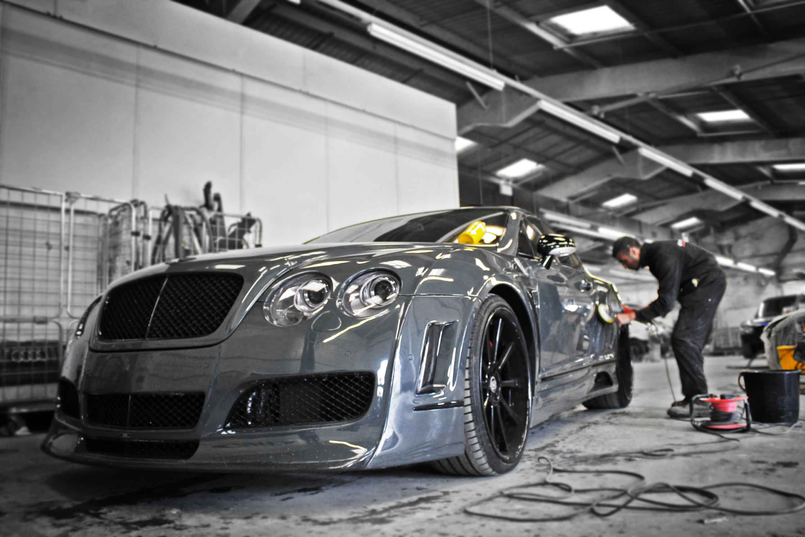 Silver modified Bentley sportscar being polished and buffed by a worker in the Enkahnz garage.