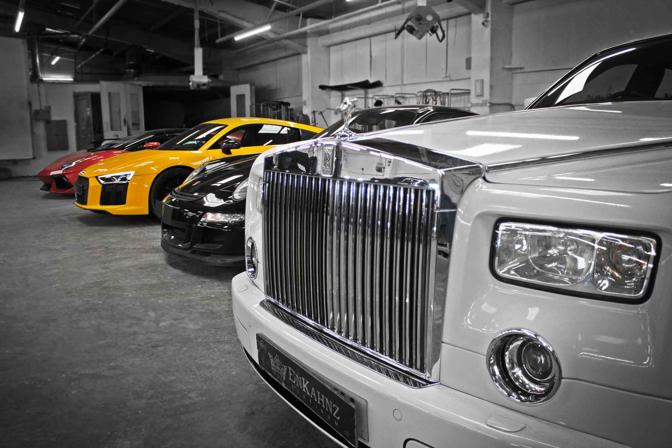 Row of luxury cars including a White Rolls-Royce Phantom, , Red Lamborghini Aventador, Yellow Audi R8 and Black Porsche 911 in the Enkahnz workshop.