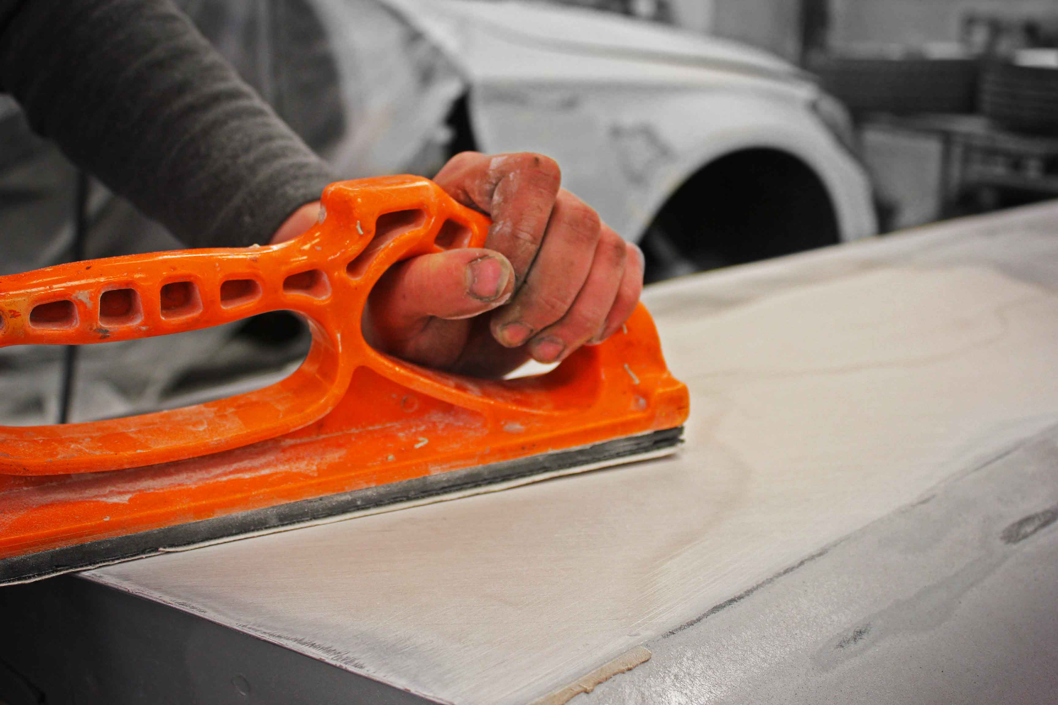 Person using an orange sanding block on a car surface. Sanding down filler. 