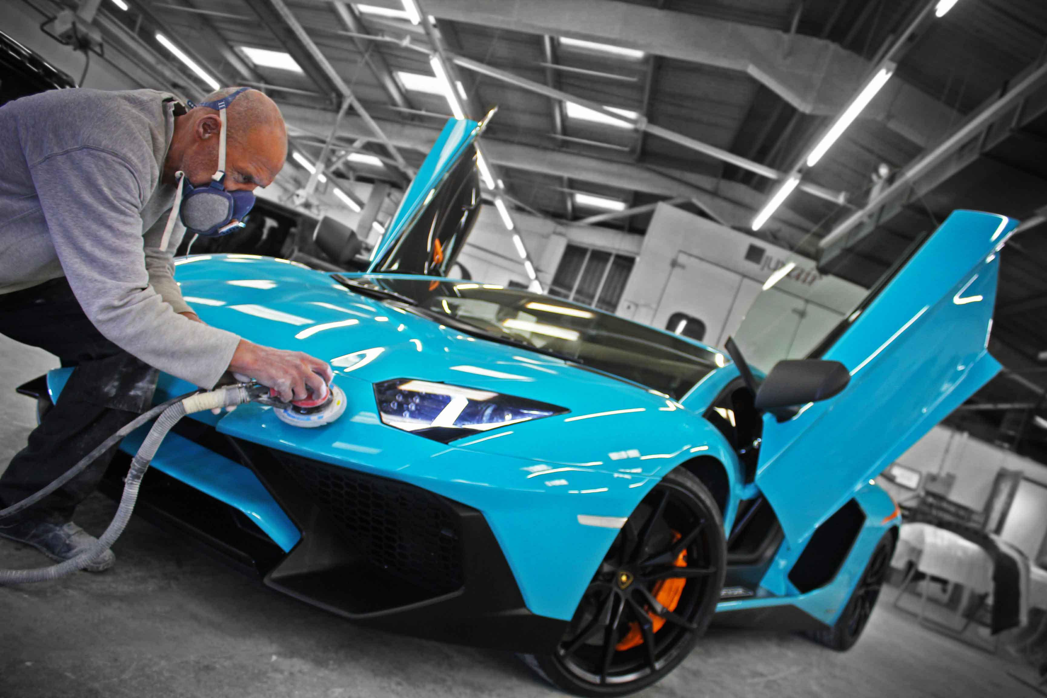 Person buffing the body surface on a blue Lamborghini Aventador SVJ supercar in Enkahnz workshop.