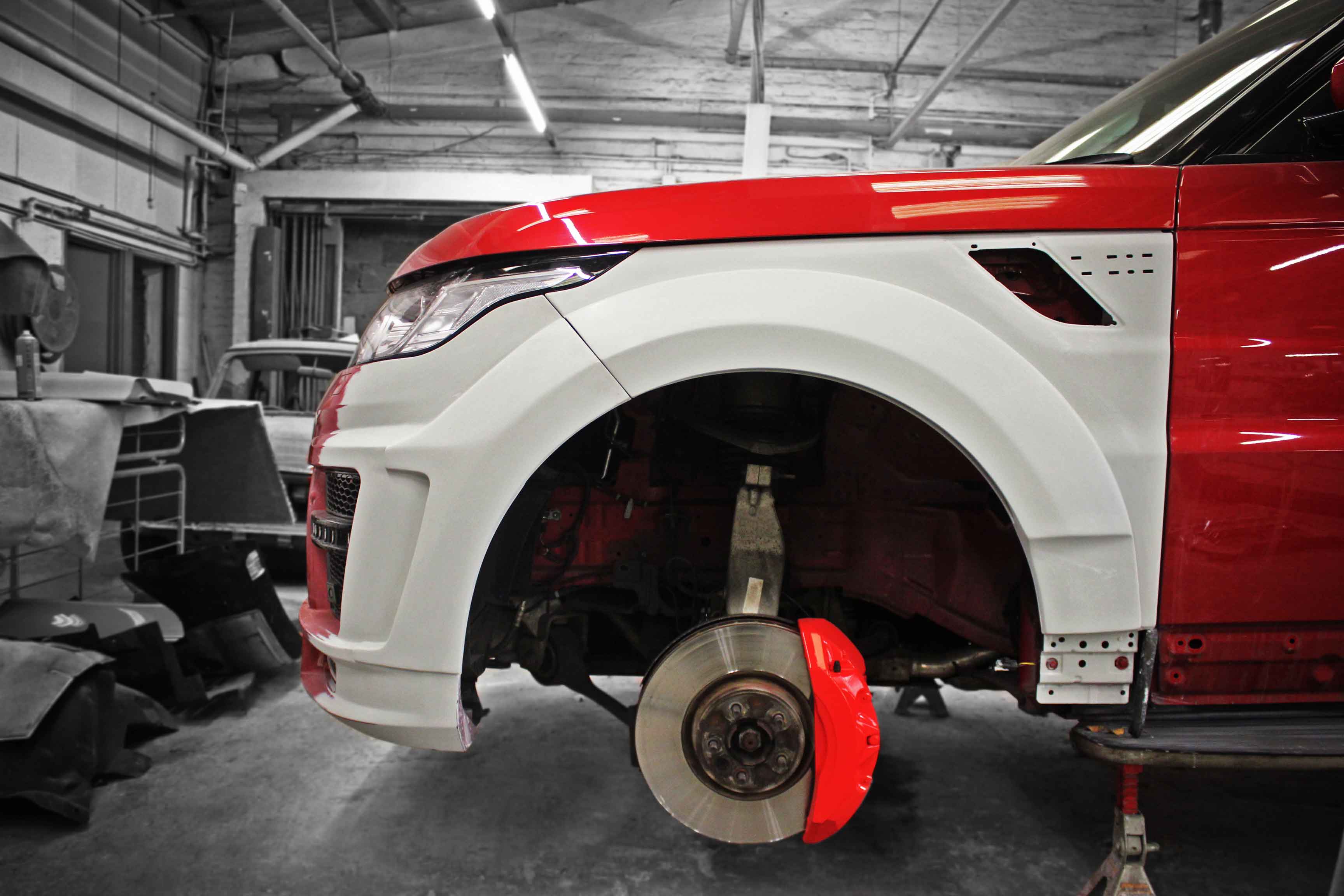 Side view close up of a Range Rover Sport L494 getting customised, fitted with modified parts lifted on jack stands in Enkahnz workshop. 
