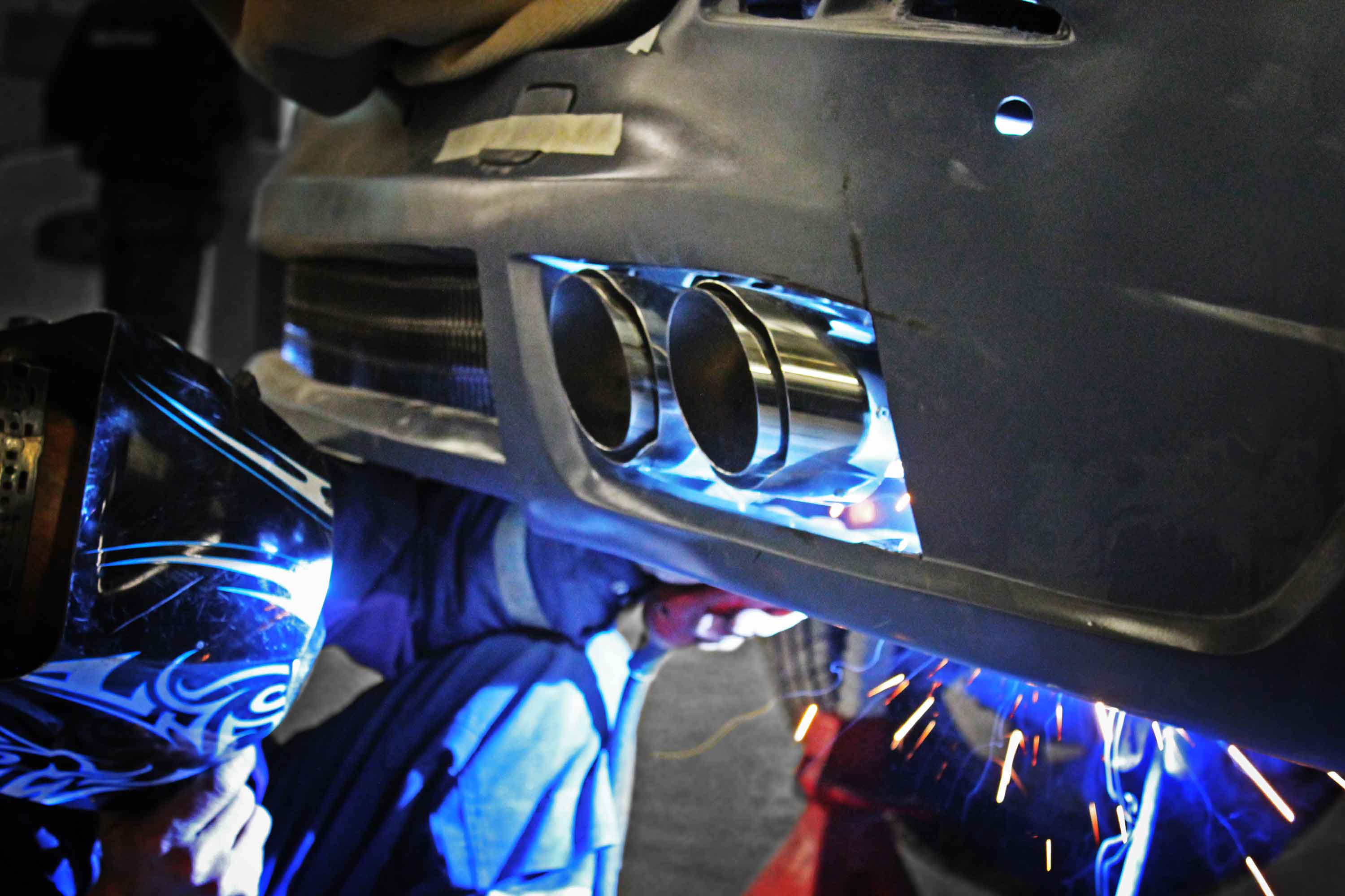 Person welding a car exhaust system with sparks flying in the Enkahnz workshop