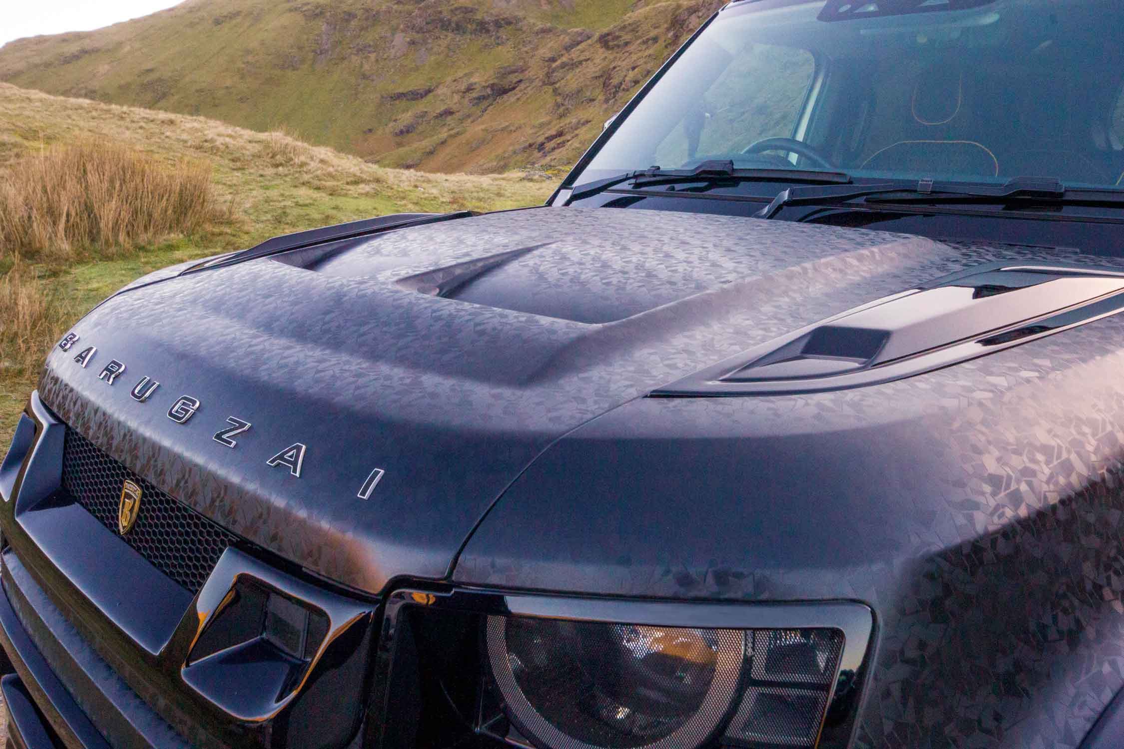 Close-up of a Land Rover Defender 110, Barugzai Falcon 007 Edition with 'Barugzai' branding on a grassy hillside.