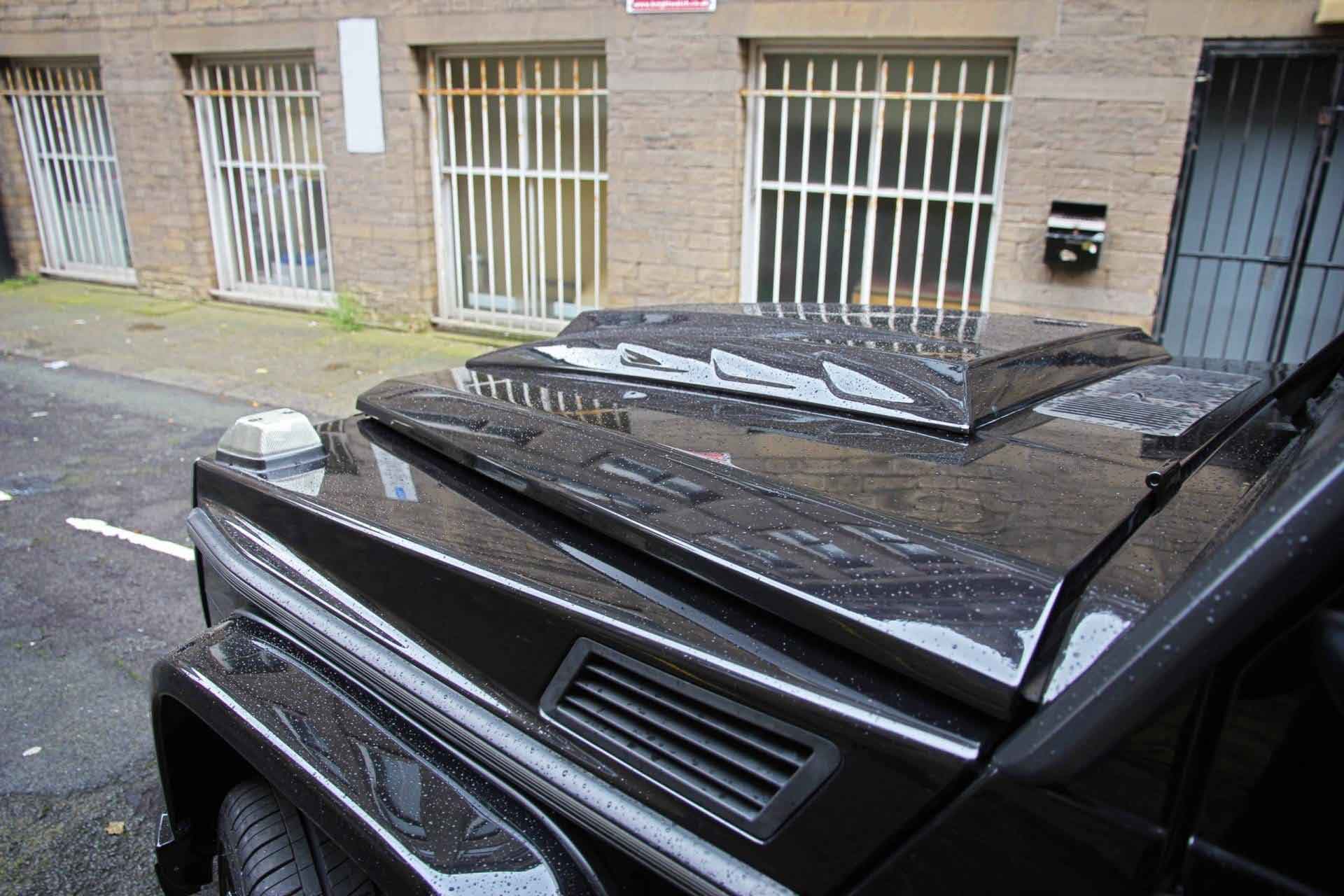 Black modified Mercedes G Wagon fitted with bonnet scoop parked in front of a building with barred windows.