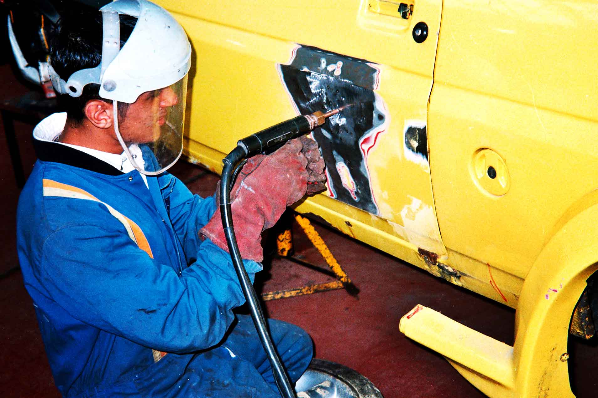 Naveed Khan working on a yellow vehicle with a tool, wearing protective gear, throwback heritage vintage shot