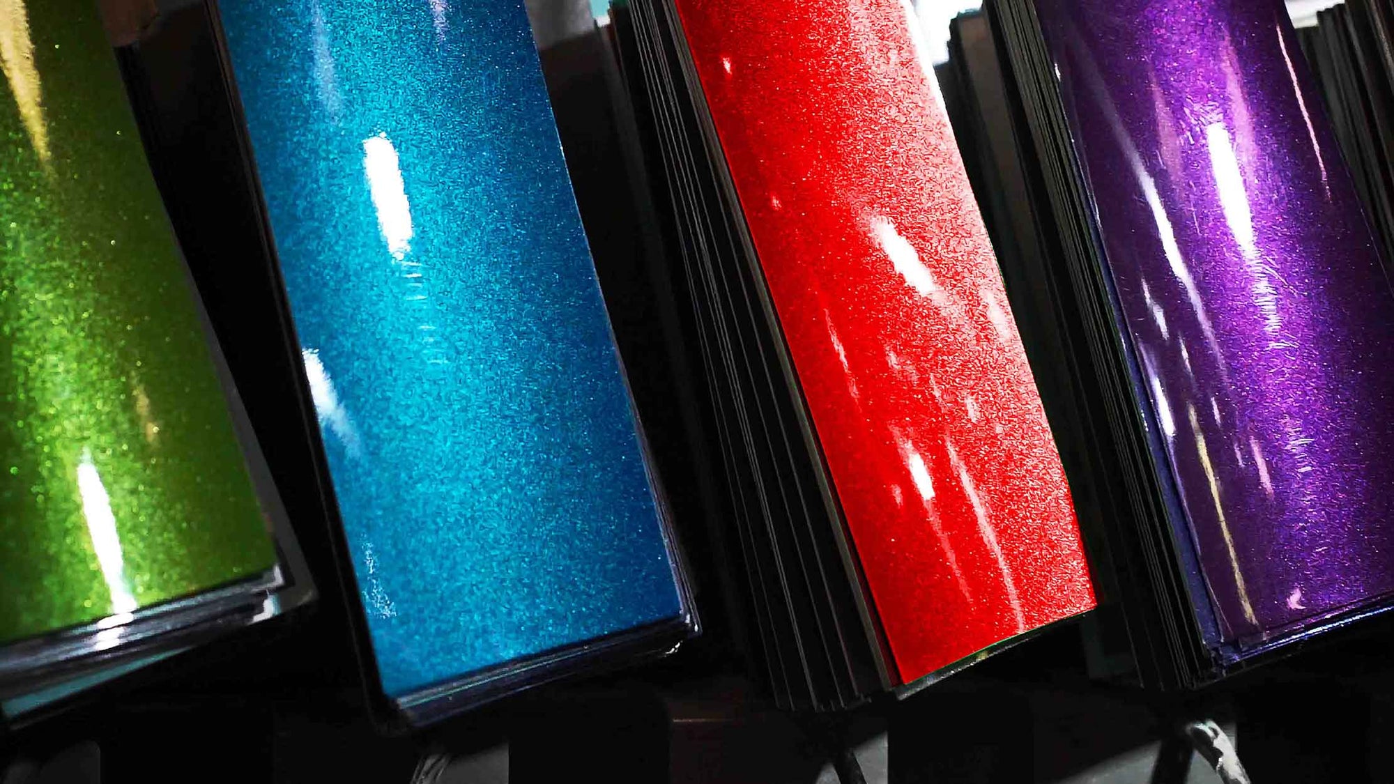 Four automotive paint swatch chips in  green, blue, red, and purple on a black background.