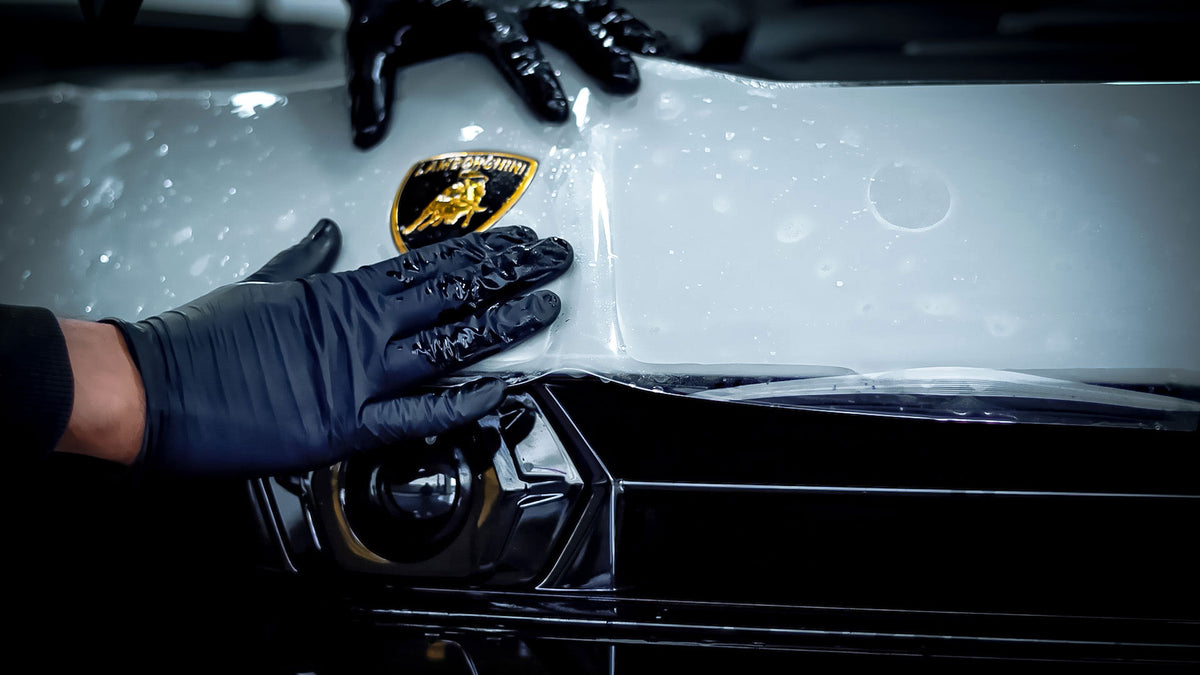 Person wearing black gloves, applying paint protection film (PPF) onto the bonnet of a Nardo Grey Lamborghini Urus