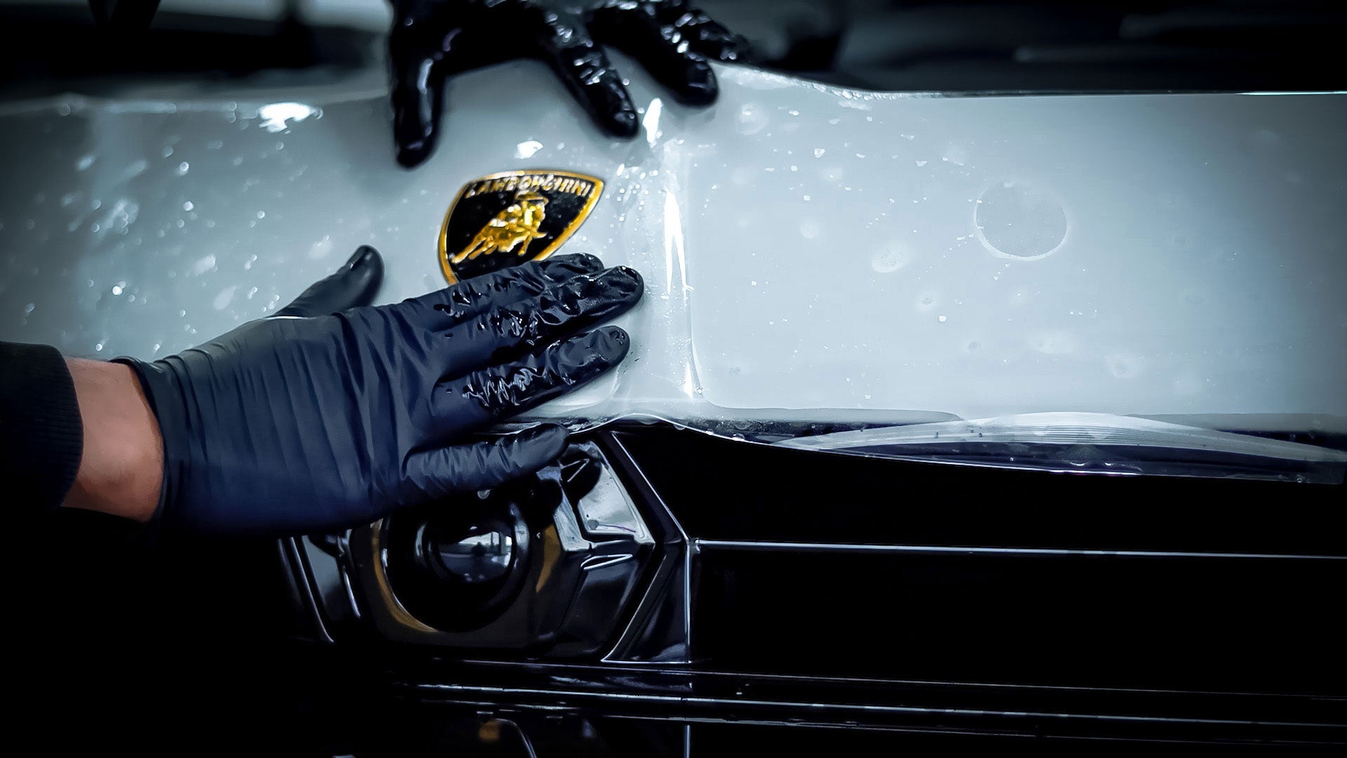 Person wearing black gloves, applying paint protection film (PPF) onto the bonnet of a Nardo Grey Lamborghini Urus