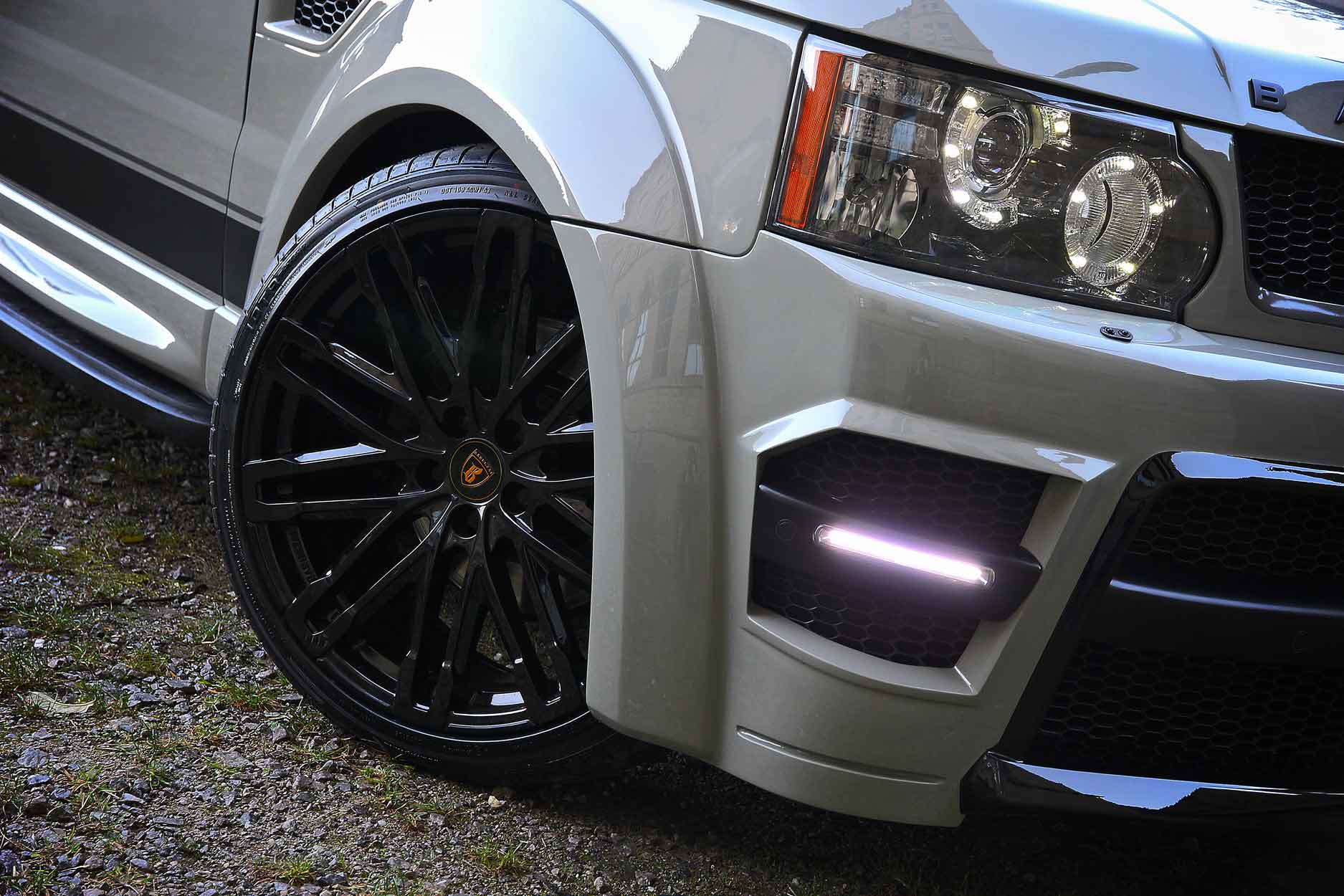 Close-up of a Range Rover Sport L320, fitted with Barugzai's Sport Classic bodykit, on a damp gravel background setting