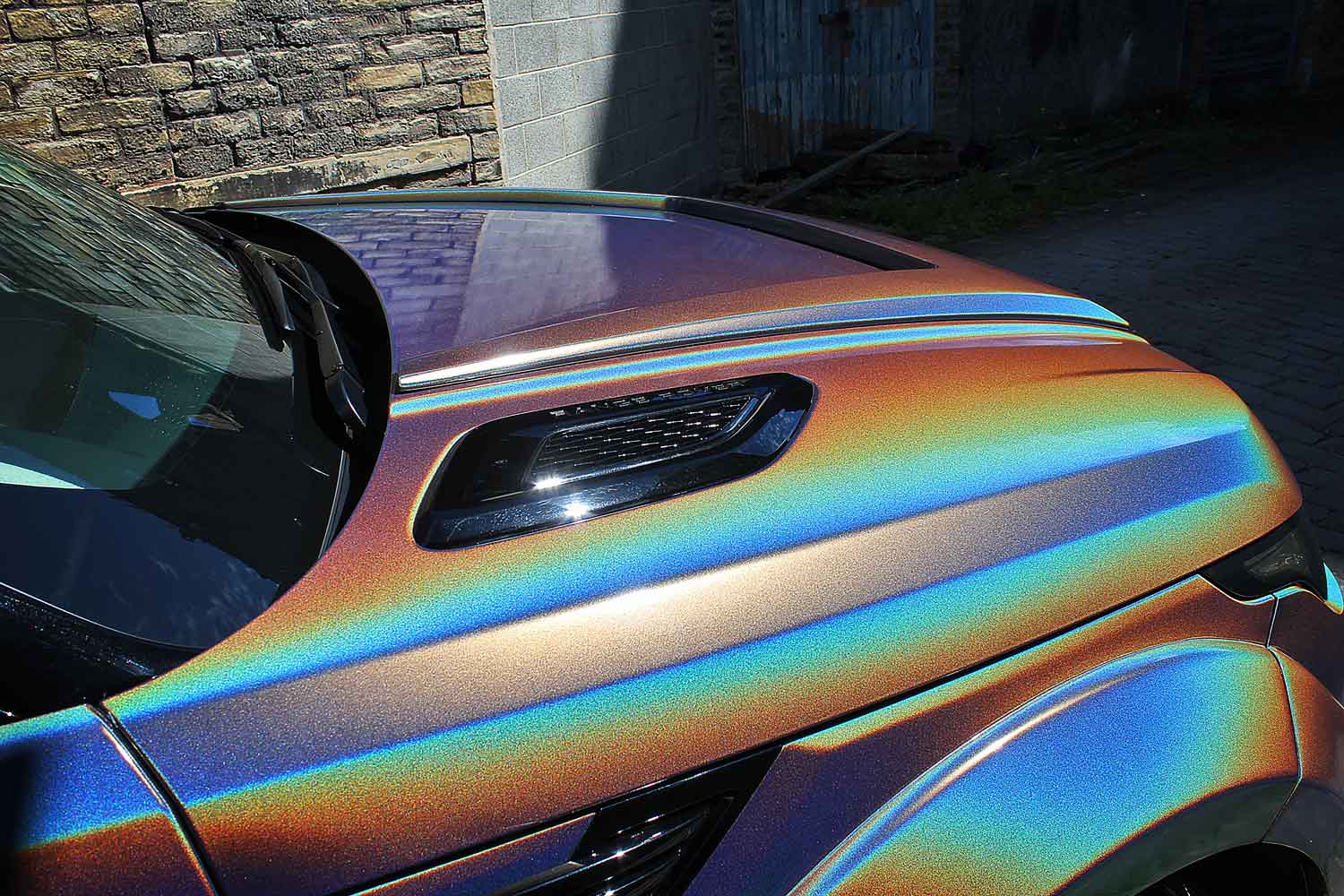 Range Rover Sport L494, fitted with Barugzai Sport Aero bodykit, with iridescent rainbow wrap parked against a stone wall.