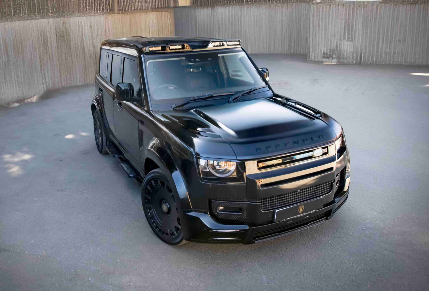 Black Land Rover Defender 110 L663, fitted with Barugzai Falcon soft bodykit parked on a concrete surface with a neutral background