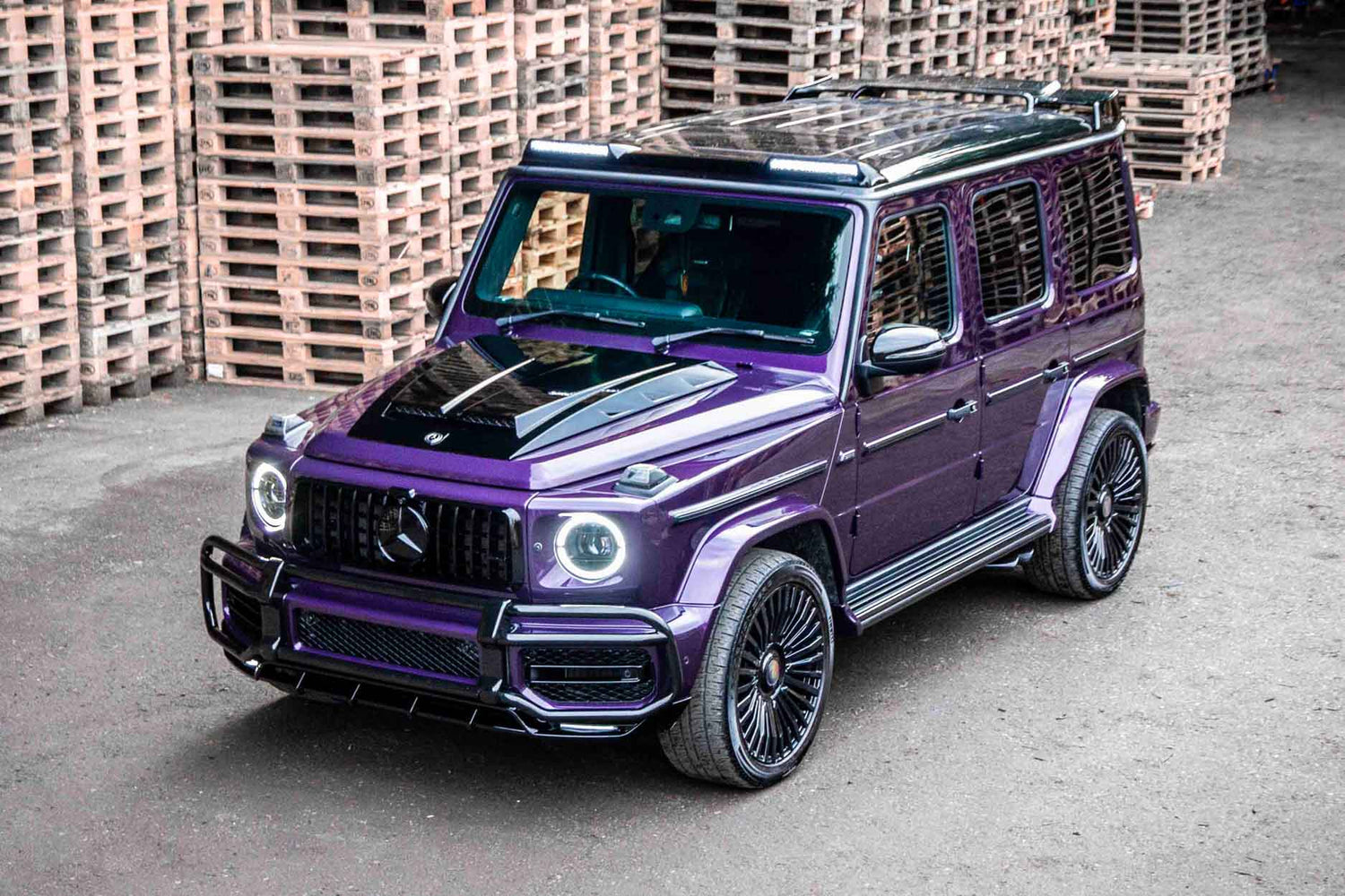 Purple Mercedes-Benz G-Class SUV parked, fitted with Enkahnz aftermarket styling accessories, on a concrete surface with wooden pallets in the background.