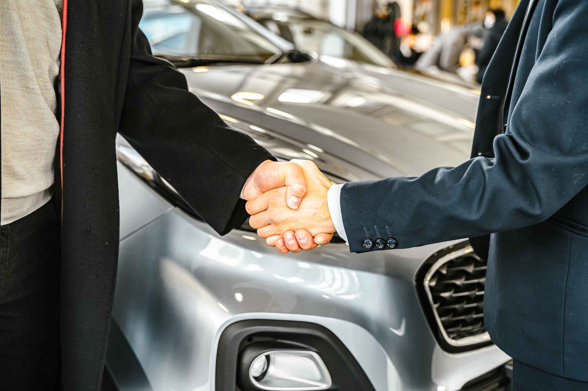 Two people shaking hands in front of a car, likely indicating a sale or agreement.