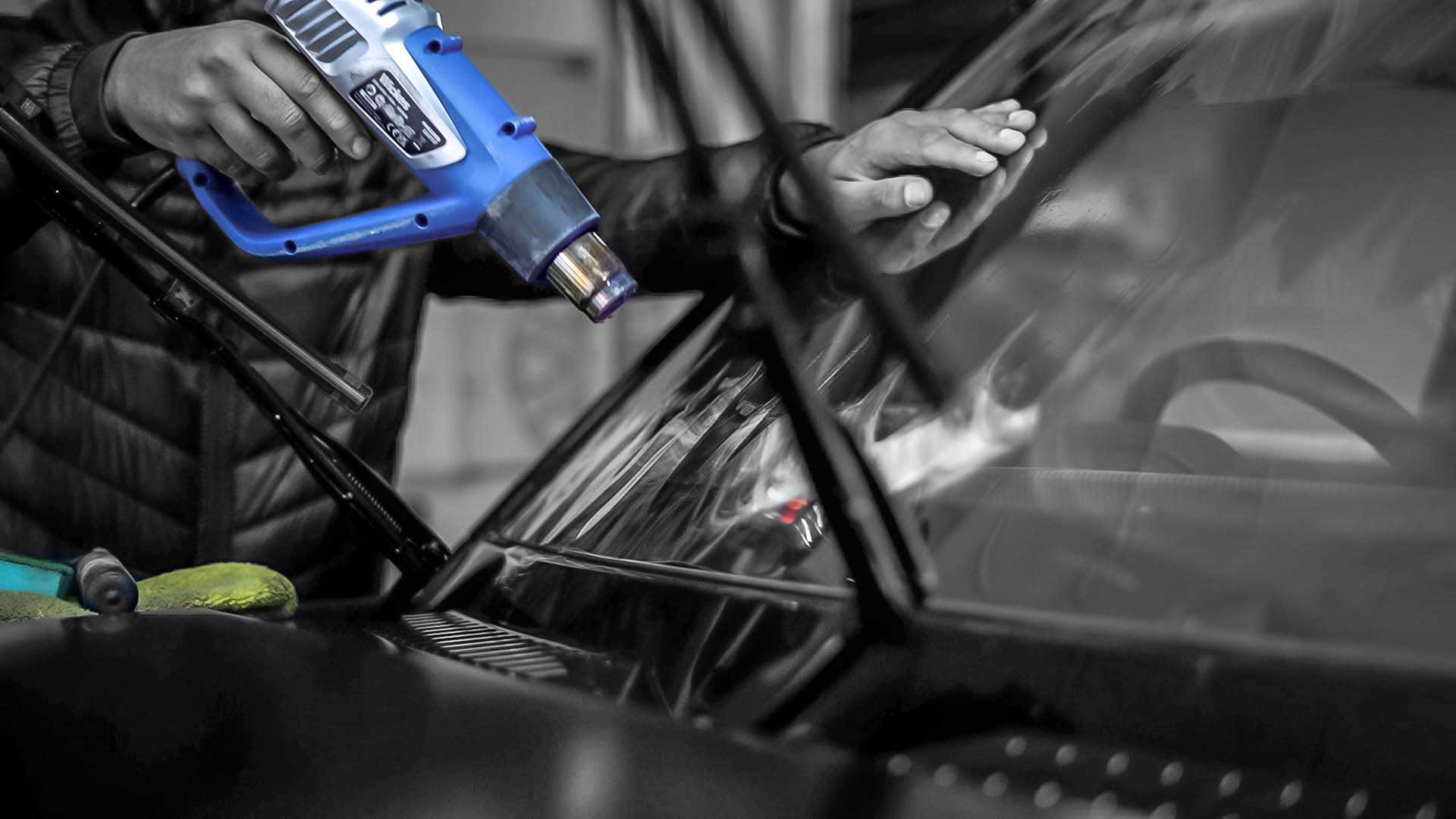 Person using a blue heat gun on a car windshield, Enkahnz privacy glass, window tinting service